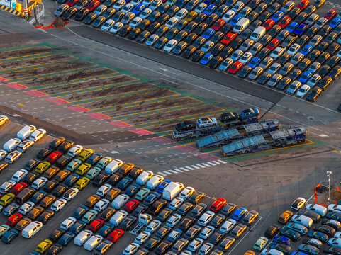 Aerial view of rows of new cars parked in a logistics port with car carrier trucks ready for transport in Civitavecchia, Lazio, Italy.
