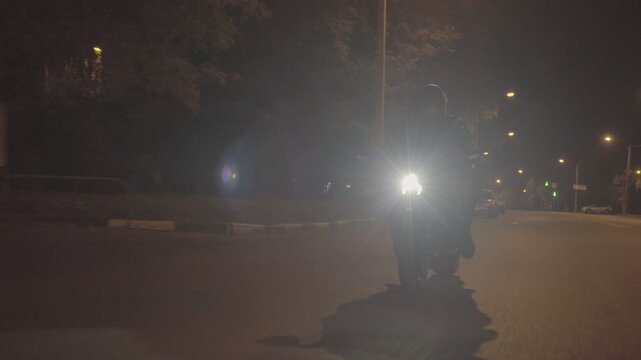 Front view of motorcyclist riding on sport motorbike with bright headlight at night. Male racer in protective moto equipment moving on his motorcycle at city street. Young man driving bike during trip