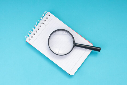 Top View of Notebook with Magnifying Glass on Blue Background