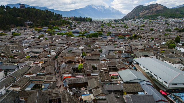 Aerial view of Lijiang Old Town with traditional grey-tiled rooftops, winding streets, and Jade Dragon Snow Mountain in the background in Lijiang Shi, Yun Nan Sheng, China.