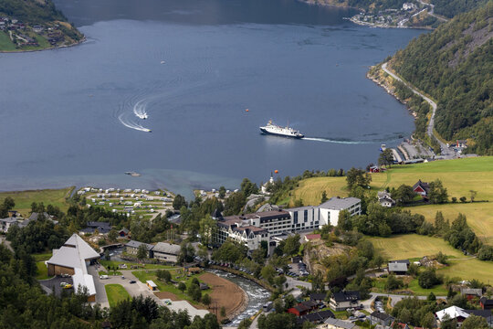 Aerial view of Geirangerfjord with a cruise ship and boats on the water, plus a hotel, campsite, and green fields along the shoreline in Stranda Municipality, More og Romsdal, Norway.