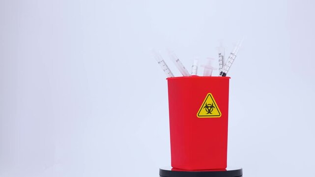 Red sharps disposal container holding used clinical medical needle waste syringe equipment evoking serious hospital safety hazard backdrop