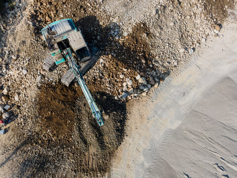 Aerial view of an excavator digging soil and moving rocks at a construction site in Karanglewas, Central Java, Indonesia.