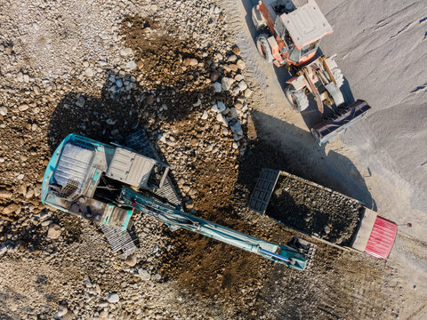 Aerial view of an excavator, a wheel loader, and a dump truck working at a gravel extraction site in Karanglewas, Central Java, Indonesia.
