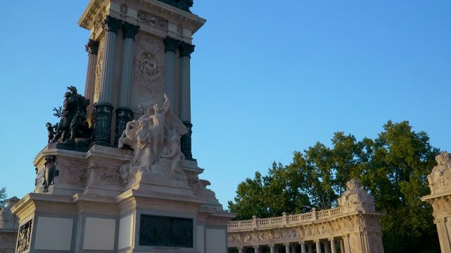 Tourists explore the historic Monument to Alfonso XII in Buen Retiro Park, Madrid, featuring neoclassical architecture and equestrian statues at sunset.