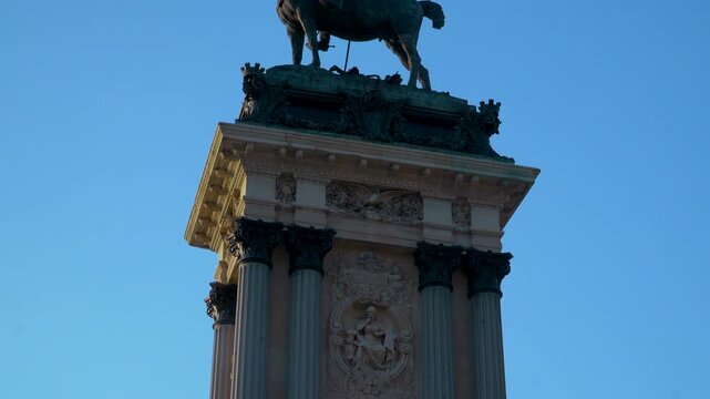 A detailed tilt down shot of the Monument to Alfonso XII featuring the equestrian statue and ornate stone carvings in Buen Retiro Park, Madrid.