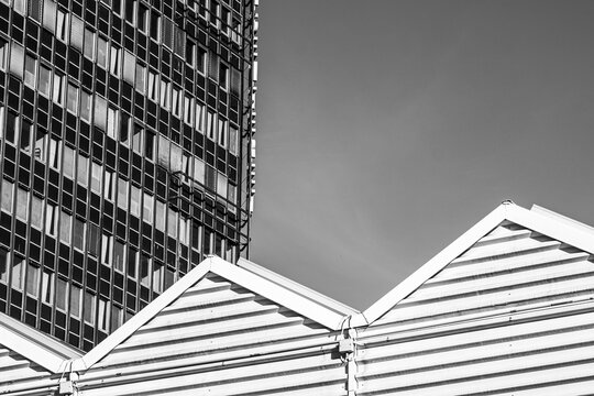 Monochrome high rise facade with geometric roof forms and a smooth gray sky creating an abstract urban composition of sharp lines and contemporary architecture