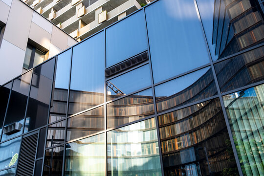 Modern reflective glass facade with blue geometric windows and sharp architectural lines creating an abstract urban composition across a contemporary building exterior