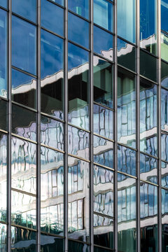 Reflective glass windows form an abstract geometric urban pattern across a modern facade with distorted buildings and sky creating layered architectural reflections