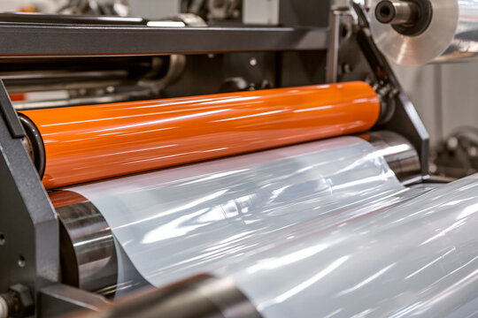 Rollers of an industrial lamination machine processing plastic film in a manufacturing plant. This scene illustrates efficient packaging material production for industrial.