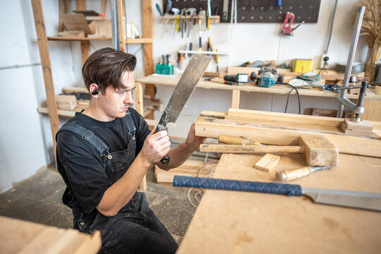 Experienced craftsman visually checking examining accuracy of cut on old wooden board at workbench, scrutiny and detailed preparation for restoration, master removing damaged area from wood with saw.