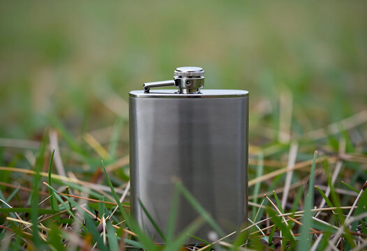 Alcohol consumption and outdoor recreation, stainless steel hip flask standing in green grass with blurred background