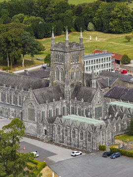 Aerial view of Mount Melleray Abbey with its prominent gothic tower, stone walls, and slate roofs surrounded by lush green fields and trees in Mount Melleray, County Waterford, Ireland.