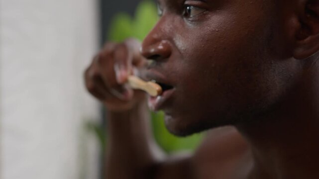 African American man brushing teeth with whitening toothpaste and toothbrush in bathroom moving shot male guy cleaning gums tooth oral care dentistry dental hygiene healthy smile fresh breath indoor