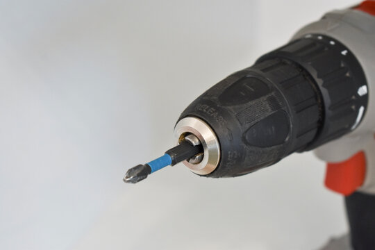 Close-up of the chuck of a grey and black cordless drill with an inserted screwdriver bit on a white background