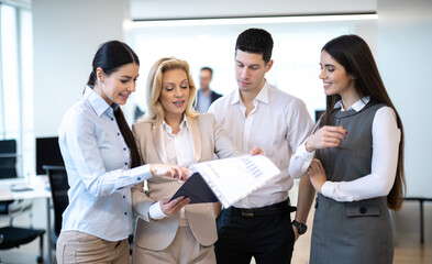 Colleagues standing together in modern office space reviewing financial document on clipboard