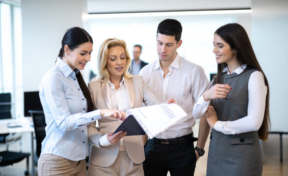 Colleagues standing together in modern office space reviewing financial document on clipboard