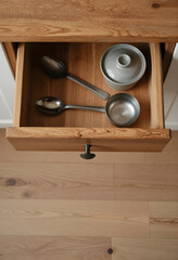 Fototapeta premium Kitchen organization and home decor, open wooden drawer with metal spoons and a small lidded pot, top-down view of kitchenware storage