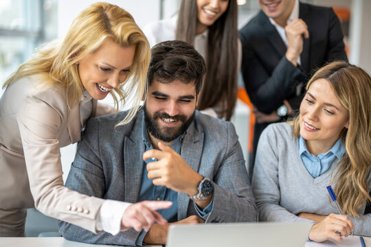 Group of happy business colleagues looking at laptop screen and celebrating success in office