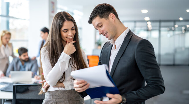 Smiling young business colleagues reviewing documents on a clipboard in modern open-plan office