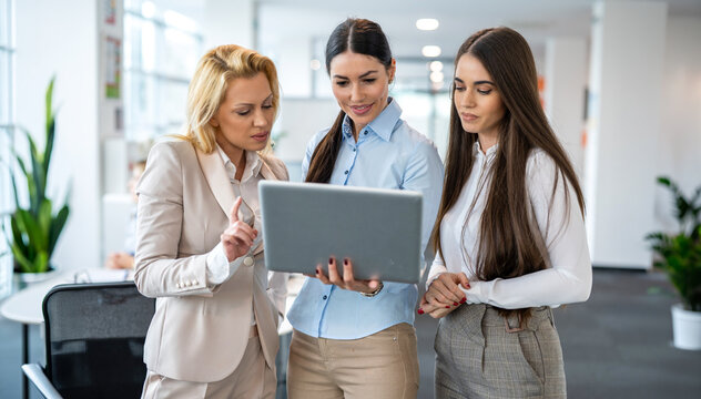Team of diverse businesswomen focusing on laptop screen and discussing project data in office