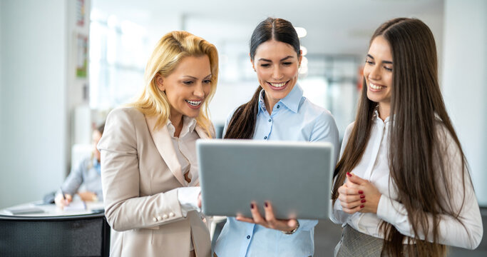 Group of cheerful businesswomen looking at laptop screen and smiling in modern office
