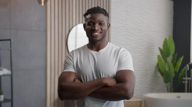 Happy African American man smiling in hotel bathroom with crossed hands pose confident male guy looking at camera with toothy smile morning routine hygiene dental health oral care inside home bath
