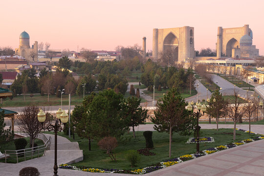 Bibi Khanym Mosque rising above a landscaped park in Samarkand at sunset. Panoramic view of the historic city with flower beds and green trees in the foreground. Ideal for travel guides and tourism.