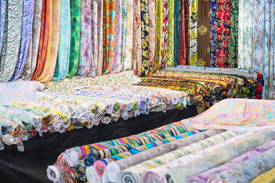Colorful fabric rolls and hanging textiles displayed at a bazaar stall in Bukhara, Uzbekistan. Vibrant assortment of patterned cloth ideal for travel, culture, and textile industry content.
