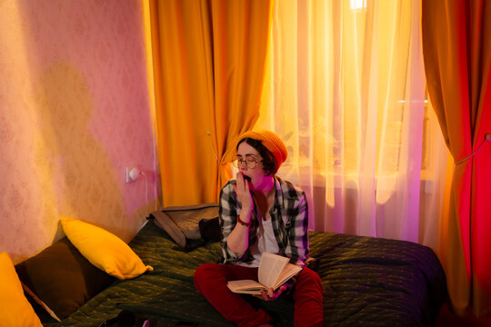Caucasian woman spends quiet time reading on bed with soft evening lighting. Comfortable setting, home education, and personal development through books. Wide shot