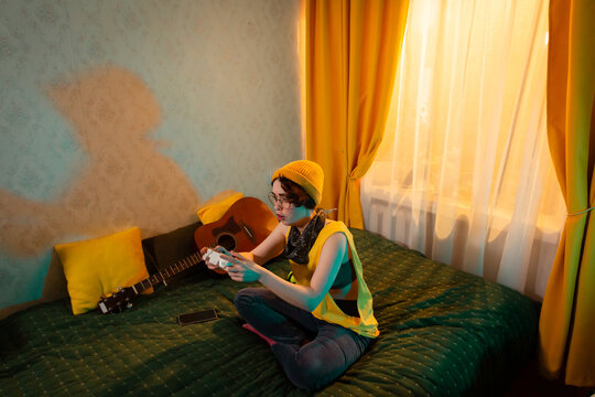 Fun loving Caucasian teenage girl gaming in her room. Sunset behind her, warm colors around. Concept of independence and screen based entertainment. Top view