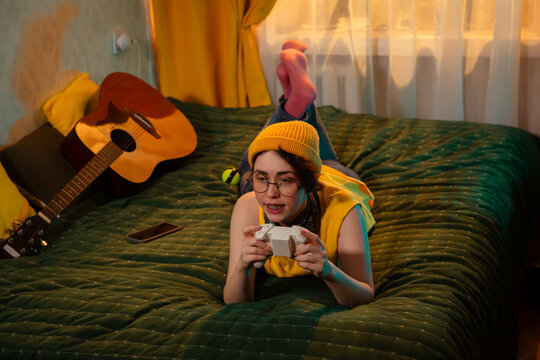 Teen girl with playful look enjoys gaming on her own at sunset. Concept of digital relaxation and expression. Wide shot, top view