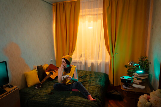 Teenage girl in casual boyish clothes concentrates while holding a game controller. Concept of tech comfort and youth habits. Wide shot
