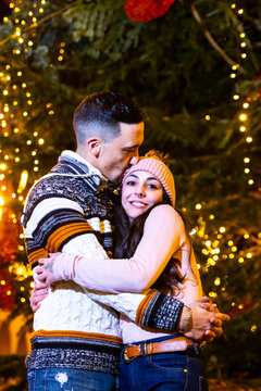 Couple celebrating christmas embracing and kissing under festive holiday lights