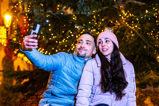 Happy couple taking a selfie with a mobile phone outdoors during christmas celebration