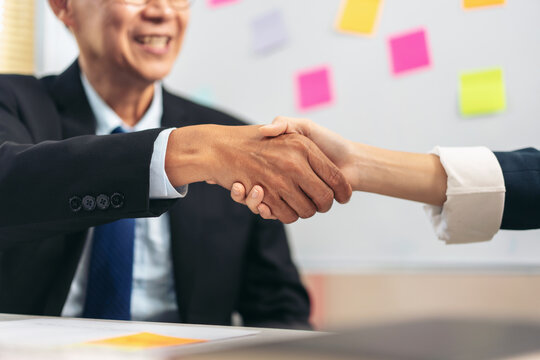 A man shakes hands with a woman in a business meeting. The man is wearing a suit and tie, and the woman is wearing a white shirt. Concept of professionalism and formality