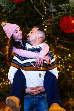 Couple celebrating christmas with piggyback ride in front of illuminated tree