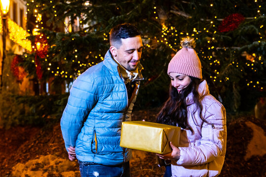 Happy couple exchanging a christmas gift at night near a decorated tree