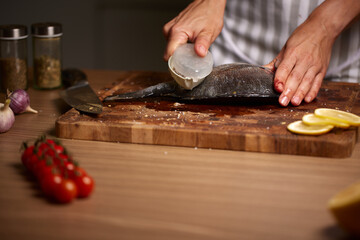 Person scaling raw fish on wooden board © Rychko Yevhen