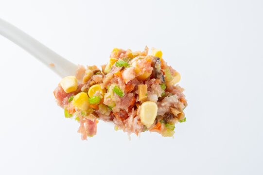 A spoonful of pork dumpling filling with corn, vegetables, and mushrooms.