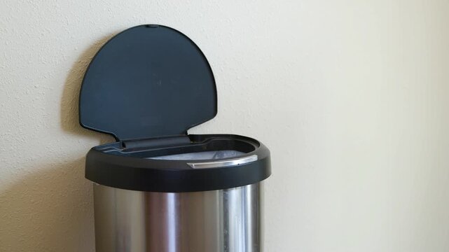 Man throws out garbage into a stainless steel trash can with automatic lid opening and closing motion.