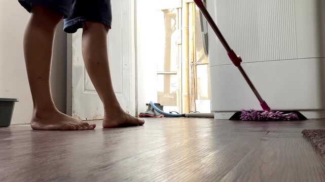 Slow motion low angle video of a housewife mopping a brown wooden floor with a purple mop. Close up view of daily household cleaning chores and domestic housework inside a home.