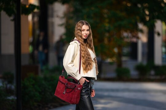 woman walking casually in urban setting with stylish leather handbag and suede jacket, side view, slightly low angle, beige and black tones, fashion street style lifestyle.