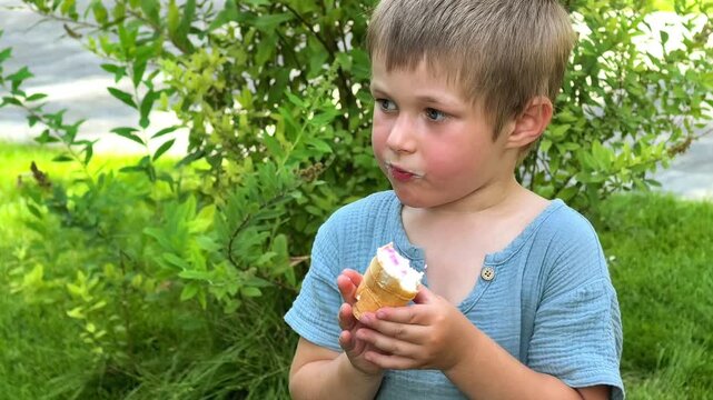 Young boy eats an ice cream cone outdoors in summer, happy childhood, sweet treat, casual snack and relaxed family leisure.