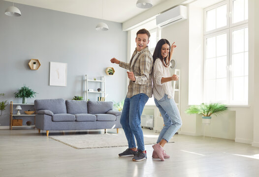 Happy family couple having fun at home. Two cheerful, joyful young people in love dancing in their spacious light living room interior in their modern house or apartment. Full body, full length shot