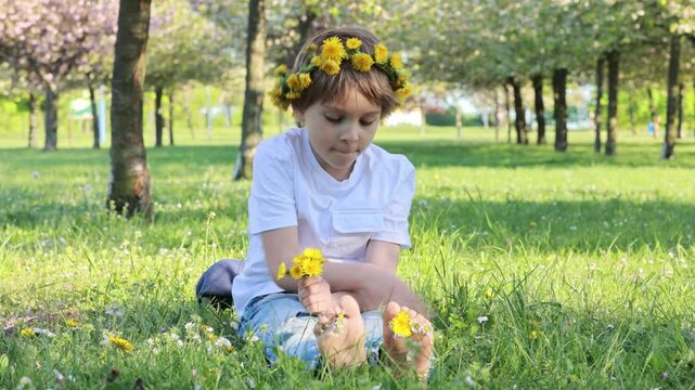 Portrait of cute stylish smiling toddler boy sitting in the grass in park