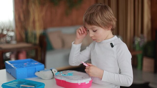Child, boy, playing with colorful dots, aquabeads, making different figures from small plastic dots