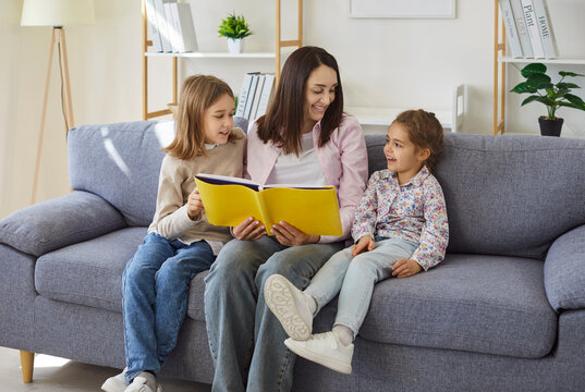 Children boy and girl enjoying leisure time with mom reading a book. Portrait of a cheerful woman mother looking through a family photo album with her kids sitting on sofa at home.