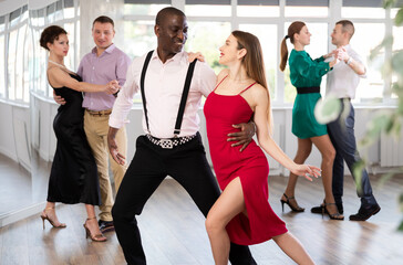 Fototapeta premium With unhurried music, woman with African man in couple spins to rhythm of waltz during lesson for novice students. Classes in mini-groups for those who want to learn dancing