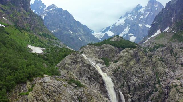 Shdugra Waterfall rises in ascending aerial view from a rocky gorge beneath Ushba glaciers near Mazeri, Svaneti, supporting trekking tourism, alpine hydrology, glacial geography, destination marketing